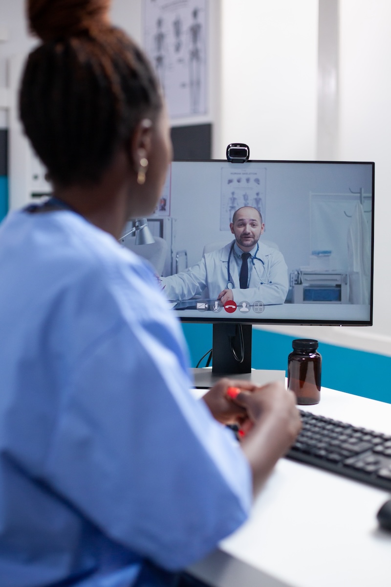 African american nurse at desk in a videocall communicating with doctor colleague in a professional medical office. Healthcare specialist doctor having online team meeting call with coworker